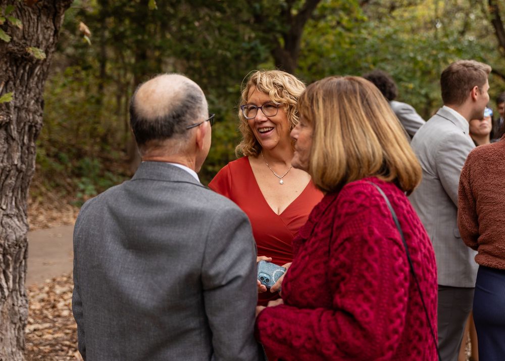 Guests socializing outdoors at a fall wedding reception among autumn trees.