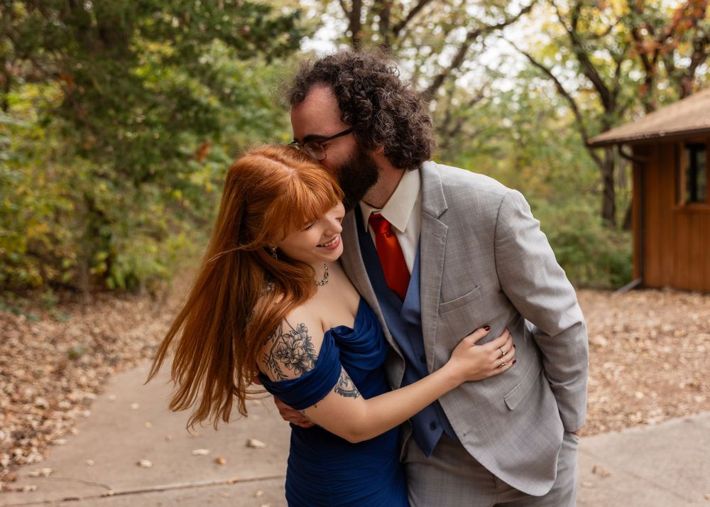 Couple embracing in fall foliage, woman with red hair and tattoos, man in gray suit with red tie at Platte River State Decker Creek Lodge