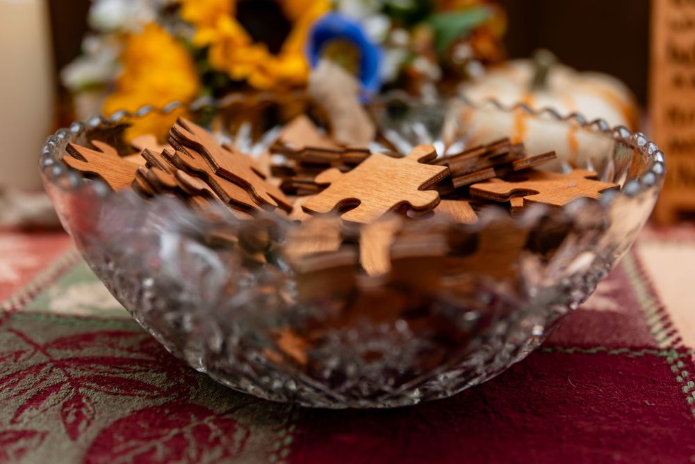Glass bowl filled with wooden puzzle pieces on a red floral tablecloth with blurred decor in background.