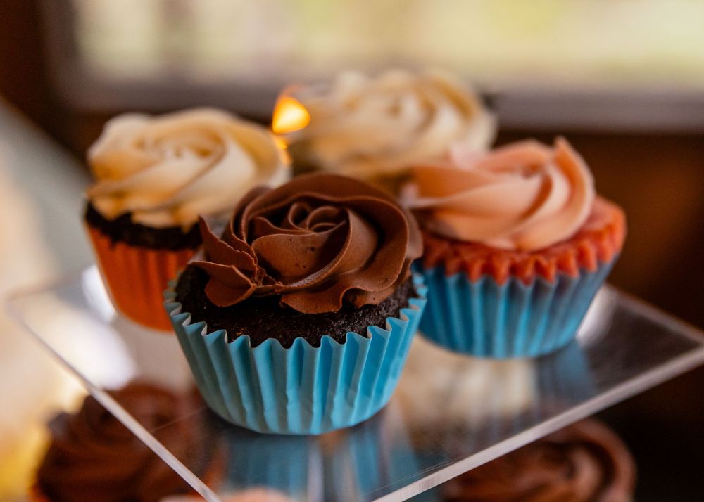 Assorted chocolate and vanilla frosted cupcakes in colorful wrappers displayed on a clear acrylic stand.