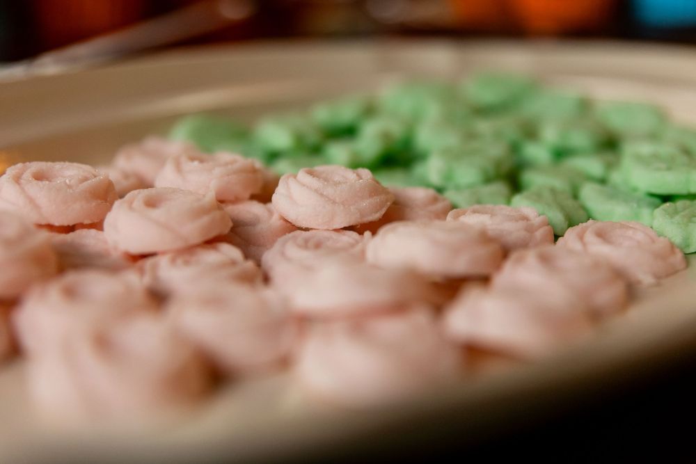 Close-up of pink and green frosted butter cream rosette cookies arranged on a plate for a wedding reception.