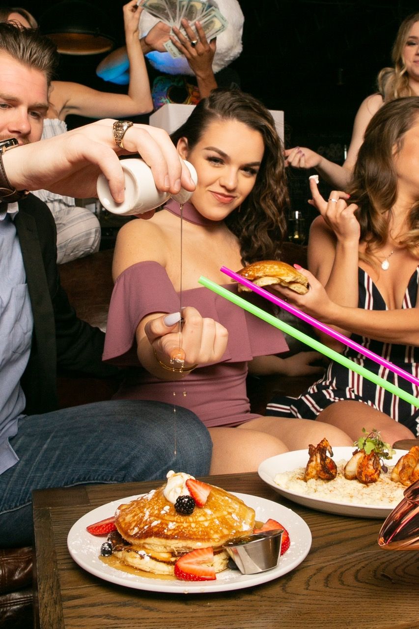 Friends enjoying a lively contemporary restaurant outing with pancakes, burgers, and colorful straws on a wooden table for brunch