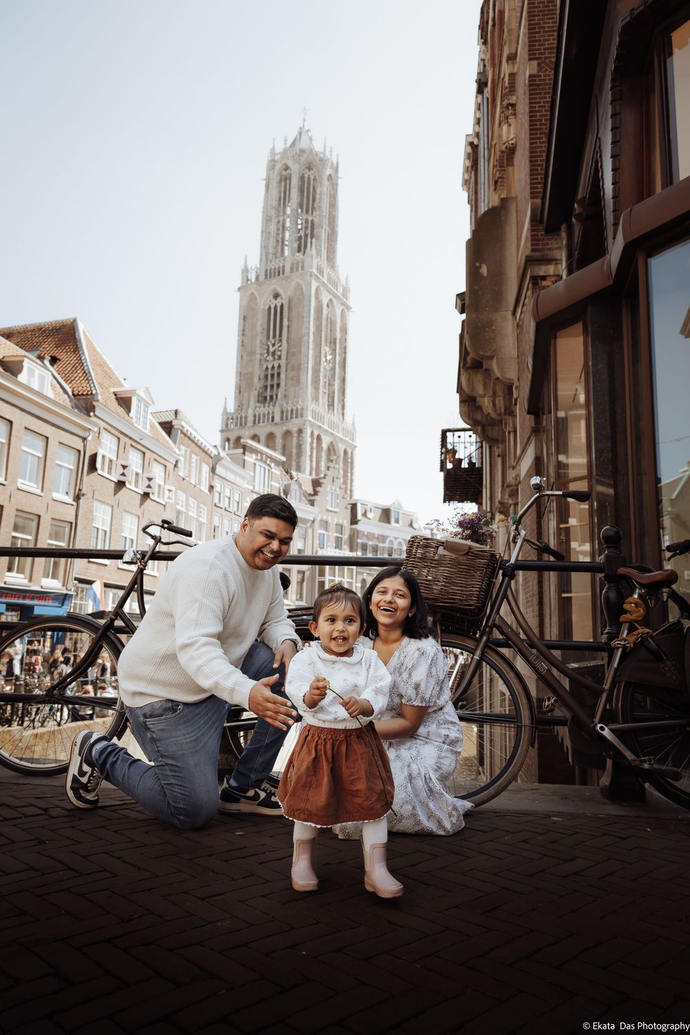 Family posing in front of Dom Tower in Utrecht, Netherlands, with bicycles and historic buildings in background.