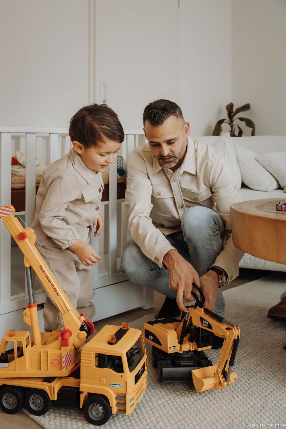 Two people playing with yellow toy construction vehicles on a carpeted floor.