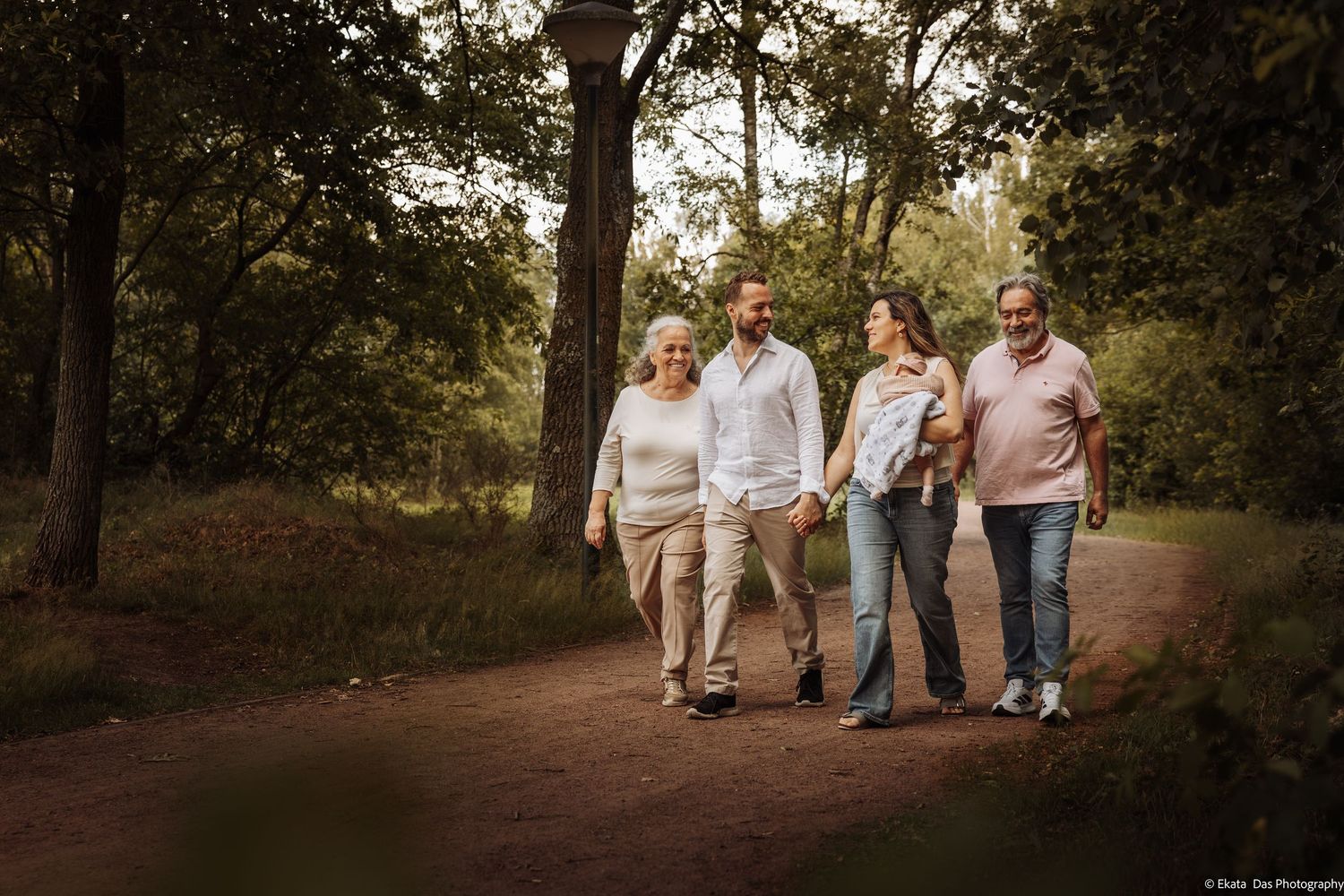 Family of four adults walking together on a forest path surrounded by lush green trees.