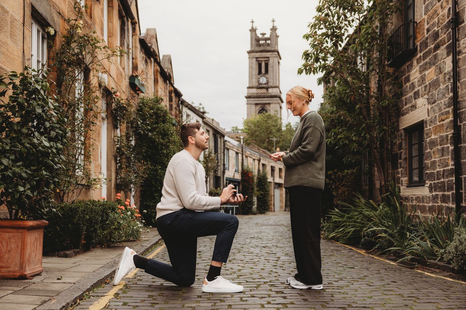 A romantic proposal scene unfolds on a charming cobblestone street in a historic European town.