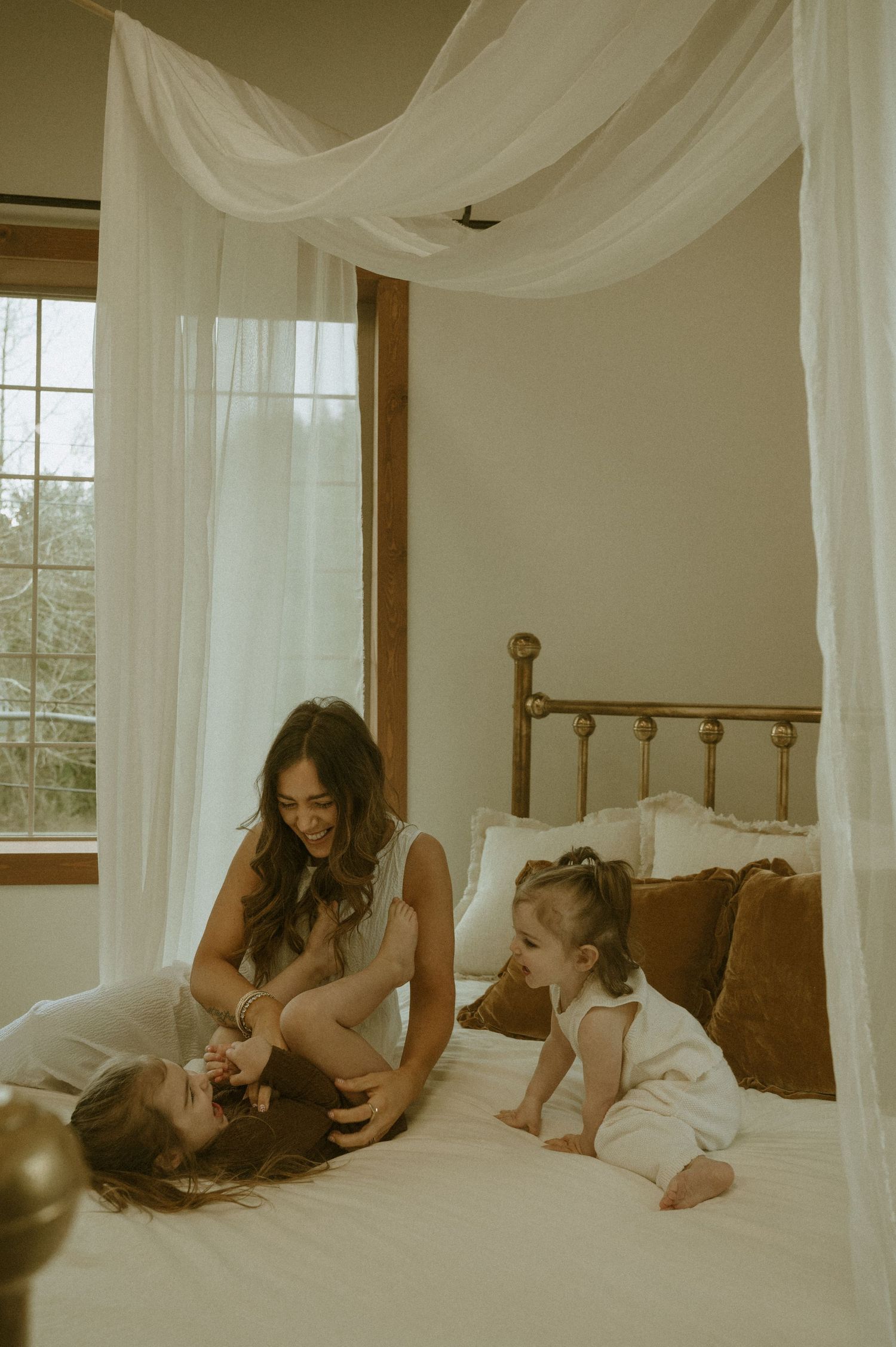 A dreamy bedroom scene with sheer white canopy drapes and natural window light creating a warm, intimate atmosphere.