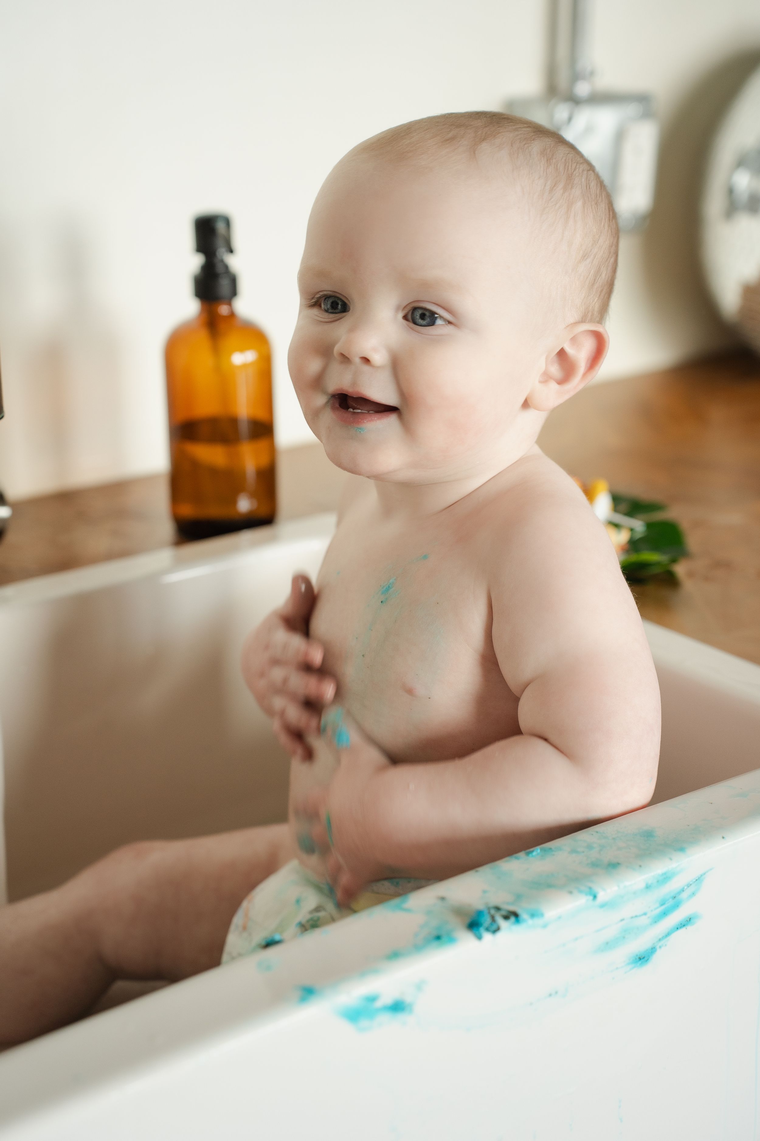 A baby in a white high chair smiles while playing with turquoise paint during a messy art activity.