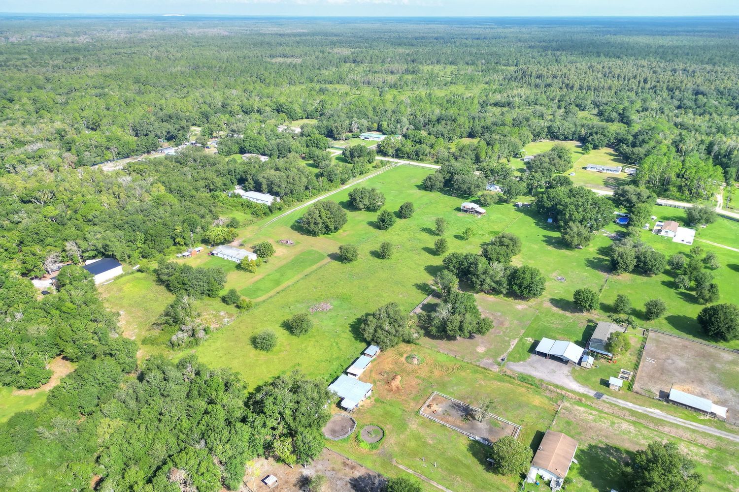 Aerial view of a lush green rural property with scattered buildings, open fields, and dense tree coverage in a suburban area