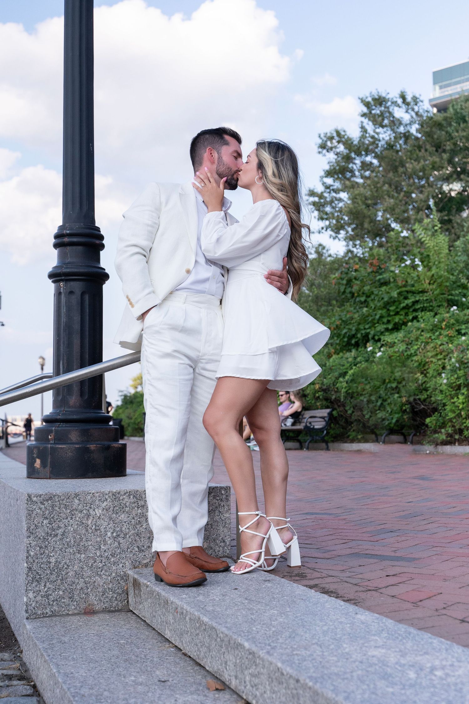 Romantic couple in matching white outfits embrace on brick steps outdoors.