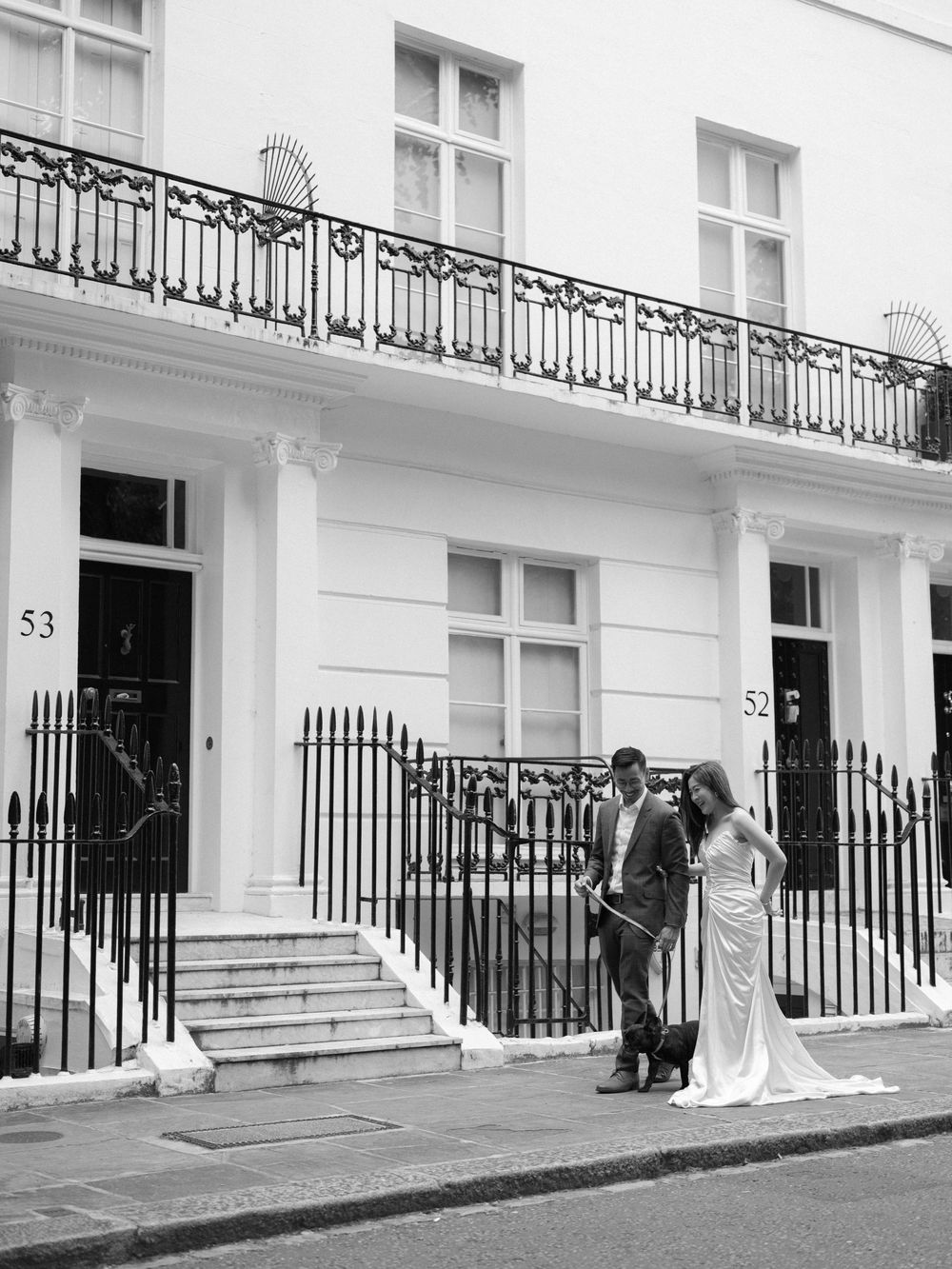 Bride and groom posing outside elegant white Georgian townhouses numbered 52 and 53 in London.