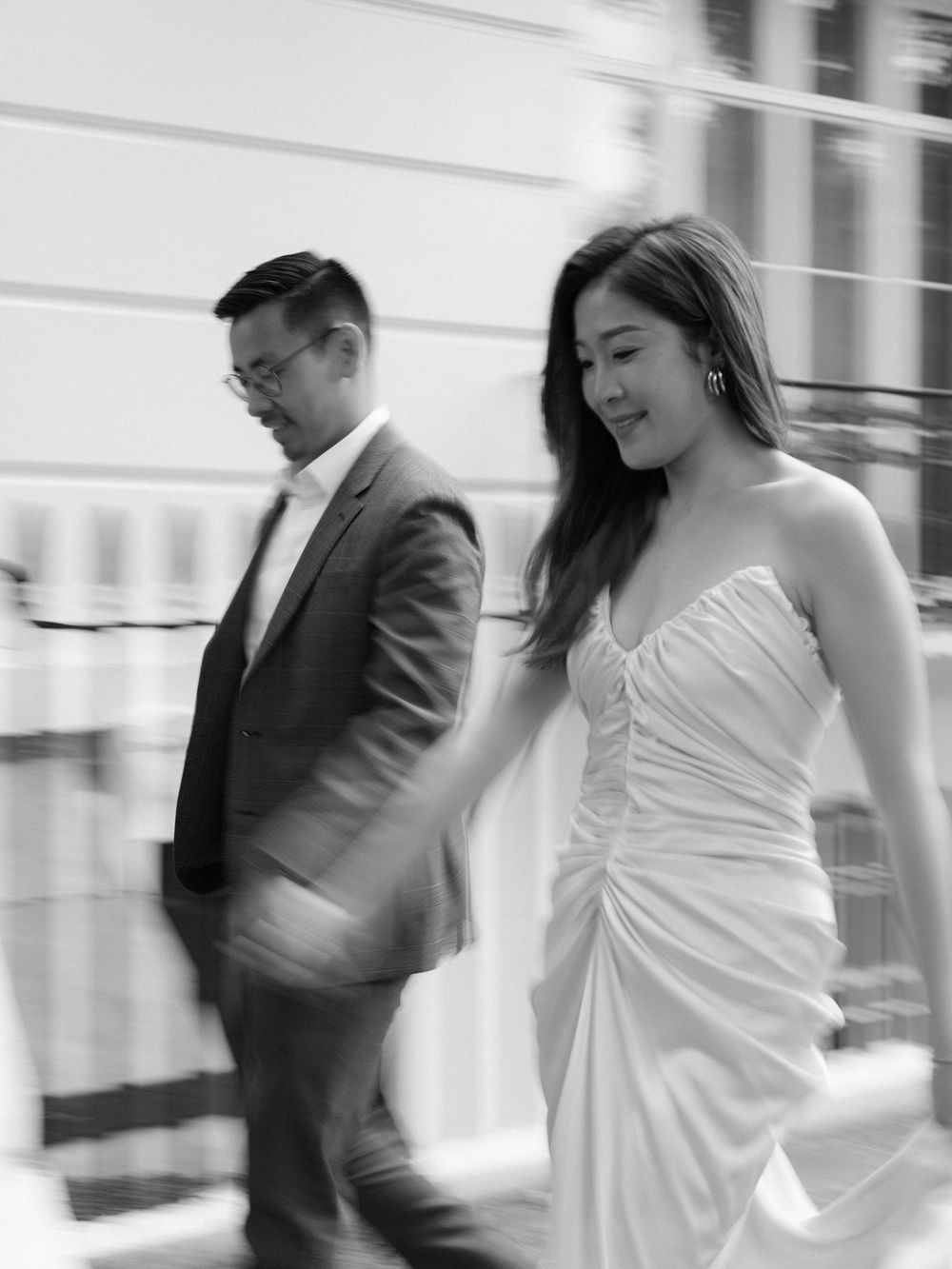 Black and white photo of a bride in a strapless gown and groom in a suit walking together.