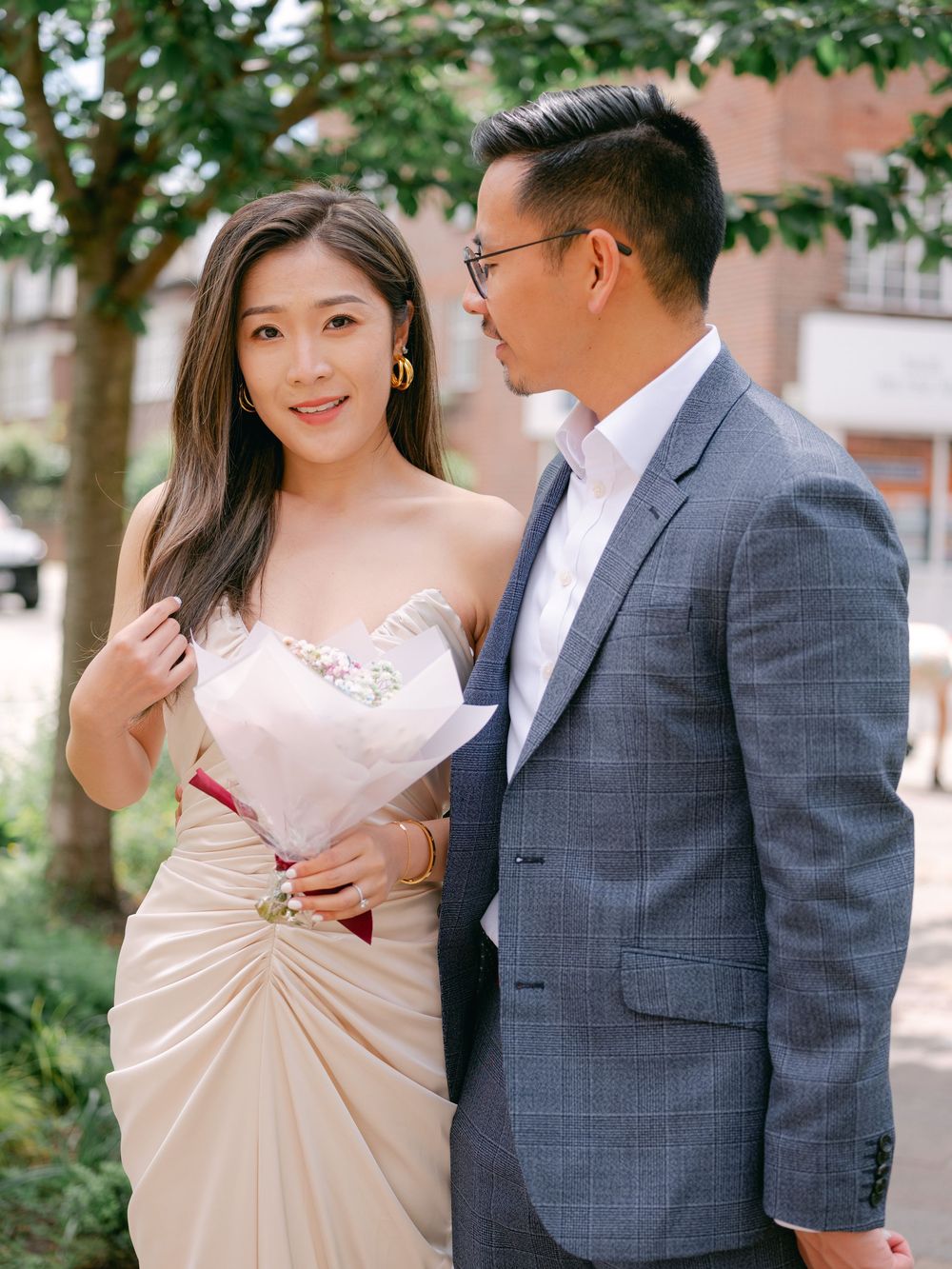 Elegant Asian couple in wedding attire share a romantic moment outdoors, bride in champagne dress, groom in grey suit.