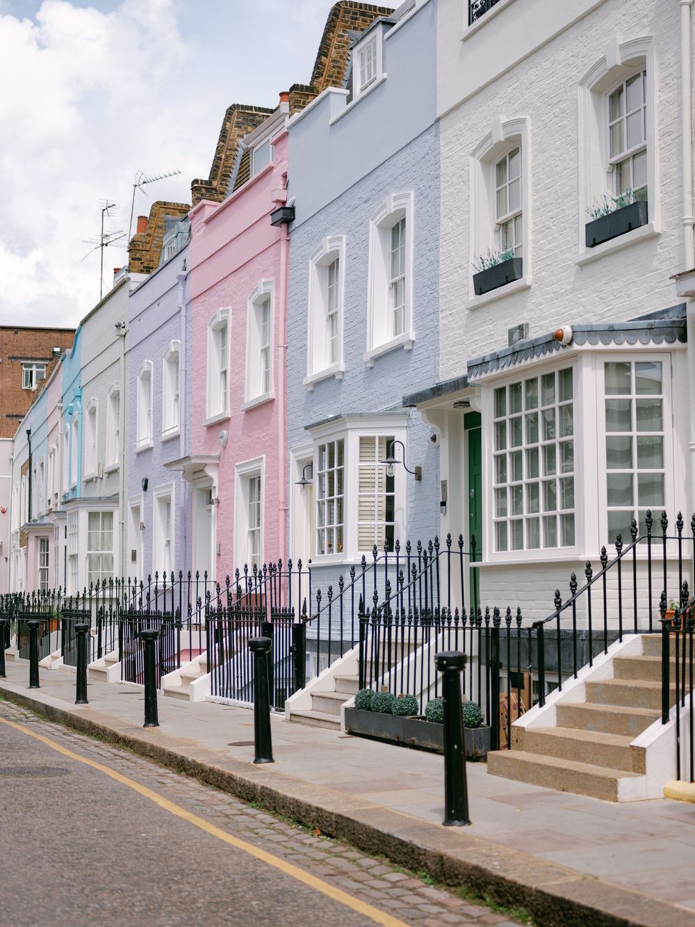 Row of colorful pastel terraced houses with black iron railings on a quiet London street.