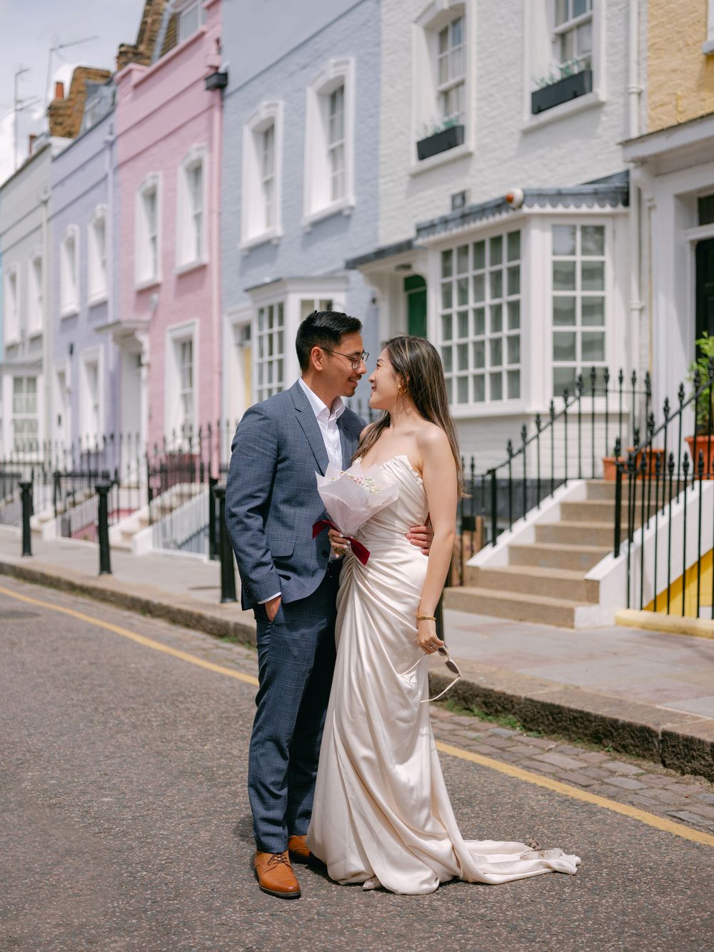 Couple in wedding attire sharing a romantic moment on a colorful street in London.