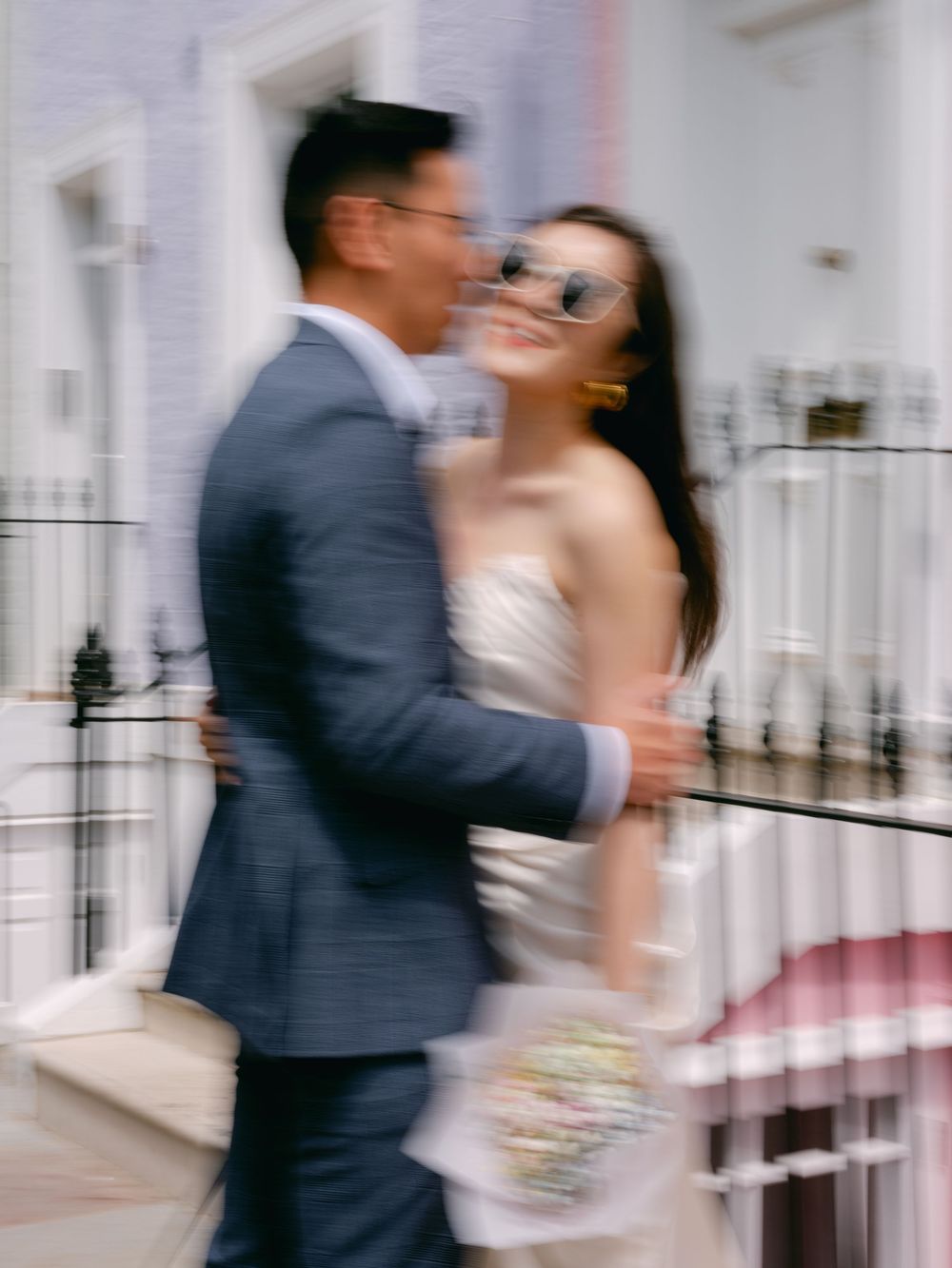 Motion blur artistic shot of couple embracing, bride in white satin dress and groom in navy suit in London.