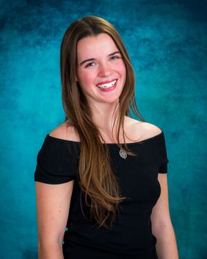 Young woman with long brown hair smiling brightly, wearing a black off-shoulder top and necklace against a teal backdrop.