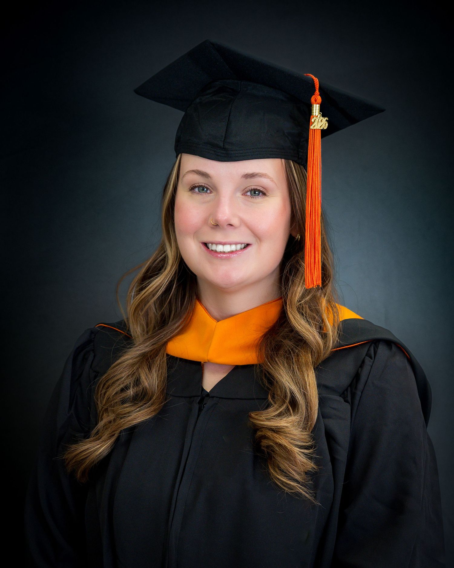 Smiling graduate in black cap and gown with orange tassel and hood poses for professional graduation portrait.