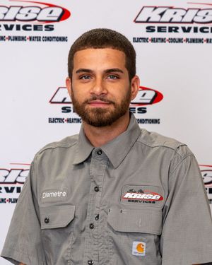Diemetre, a Krise Services technician, poses in a gray uniform shirt in front of a branded company backdrop.