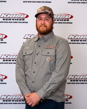 Man in gray Carhartt shirt and camo cap stands before KRIBO Services branded backdrop.