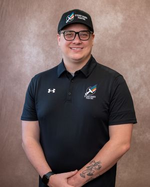 Man in black Under Armour polo and cap with tattoo poses for professional headshot.