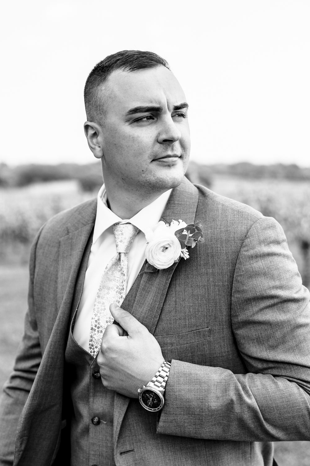 A black and white portrait of a groom in a grey suit with boutonniere.