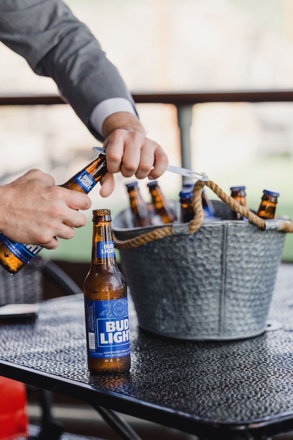 Hands opening Bud Light beer bottles from an ice bucket at an outdoor event.