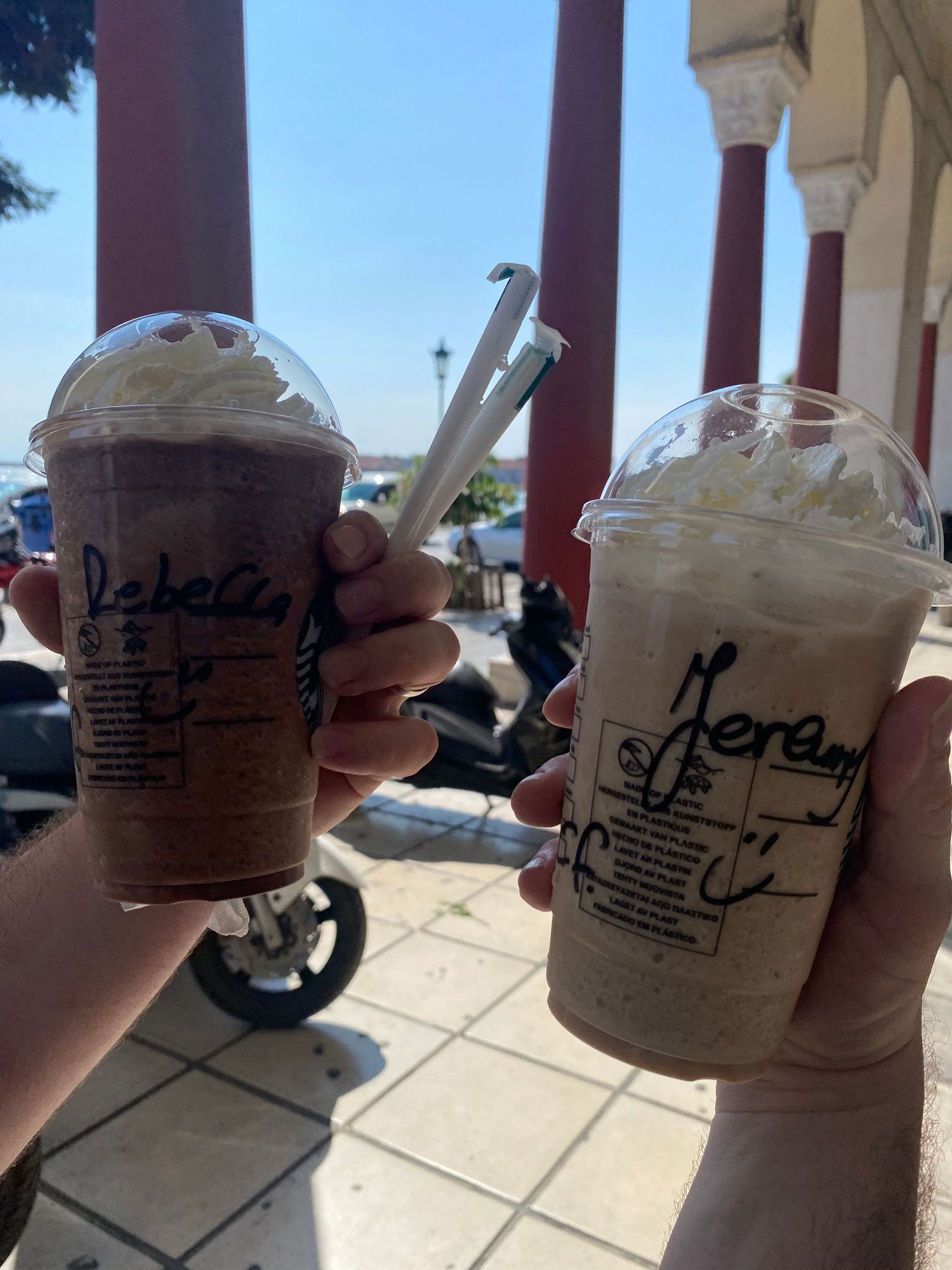 Multiple disposable coffee cups with handwritten names and markings lined up on a white surface at a cafe counter.