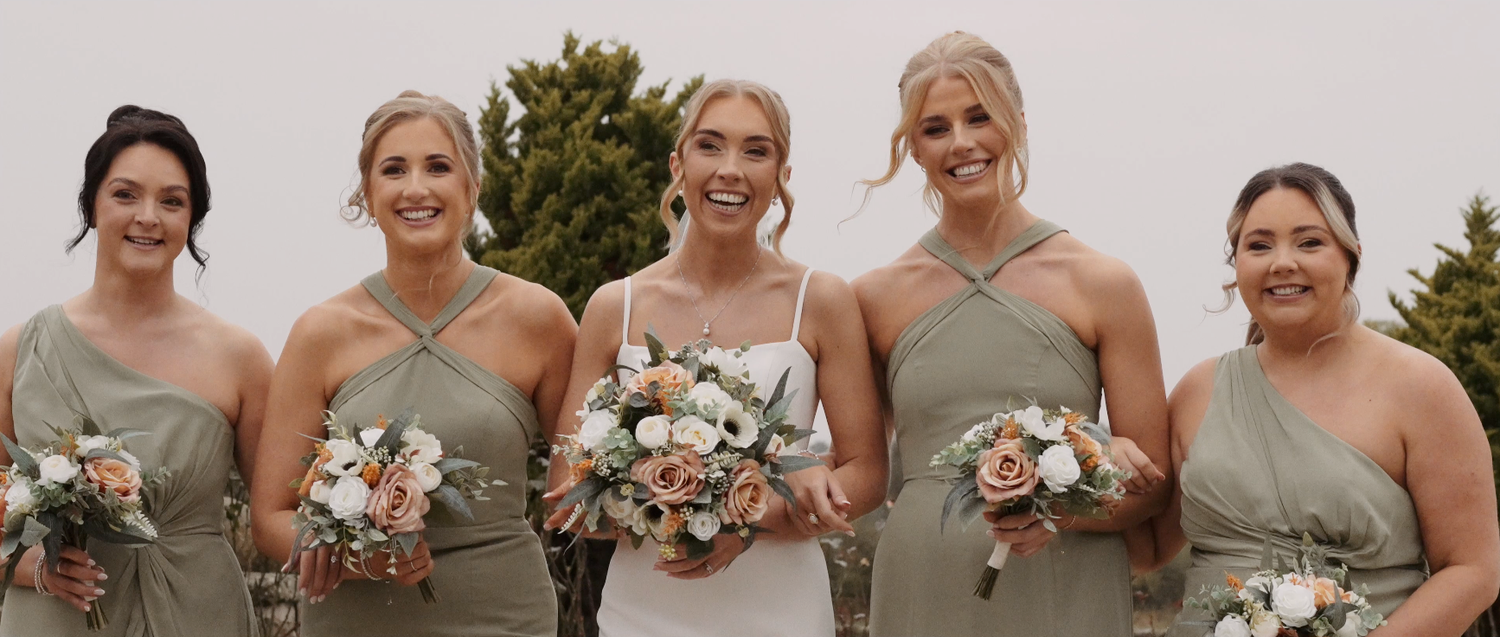 Bridal party holding white and green bouquets while wearing sage green dresses outdoors.