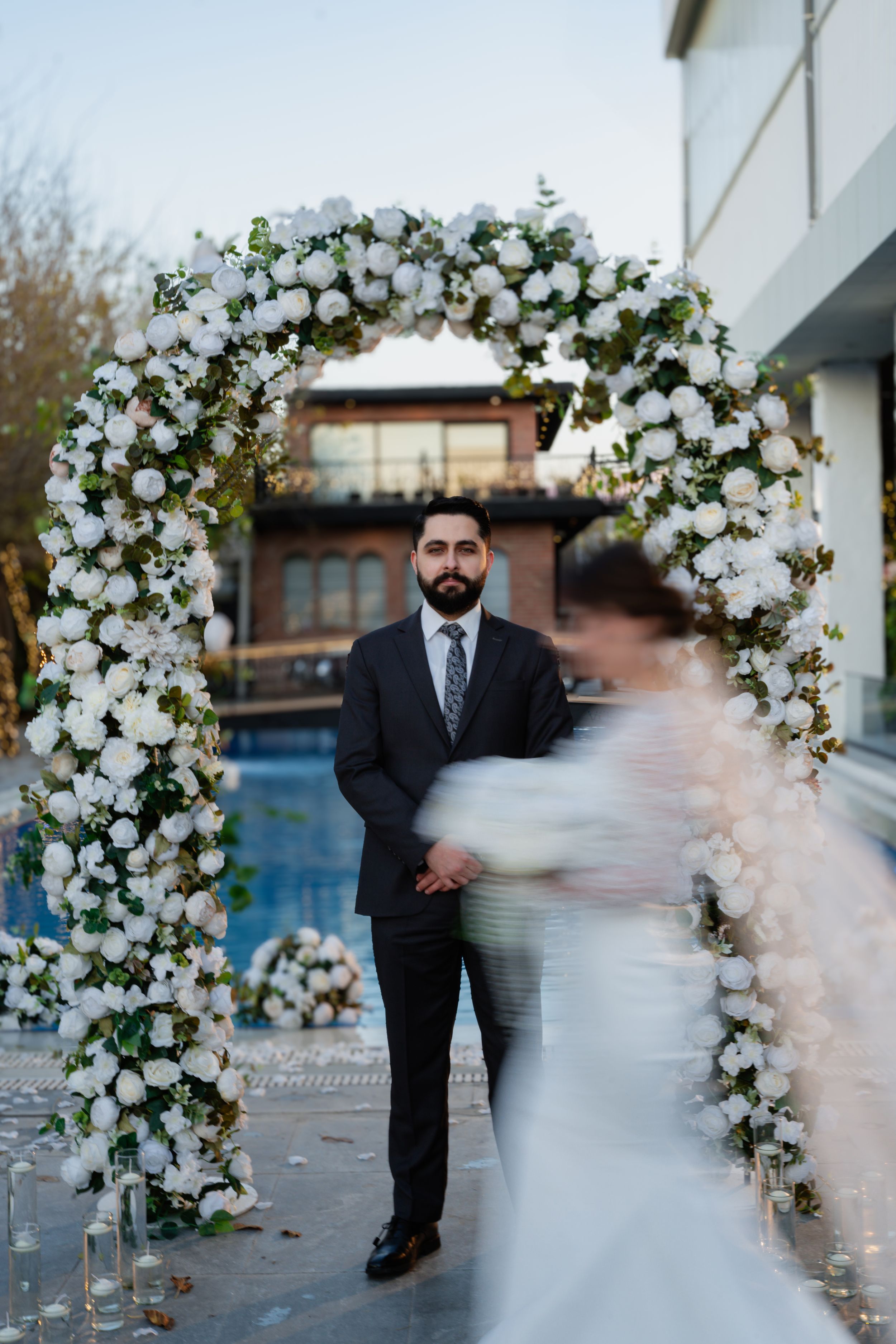Beautiful wedding ceremony setup with an elegant white floral arch and blurred movement of bride in foreground.