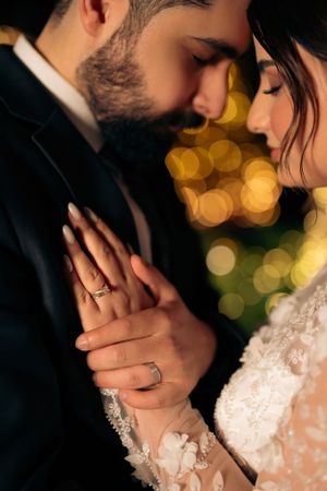 Romantic close up of a couple showing wedding rings with warm bokeh lights in the background.