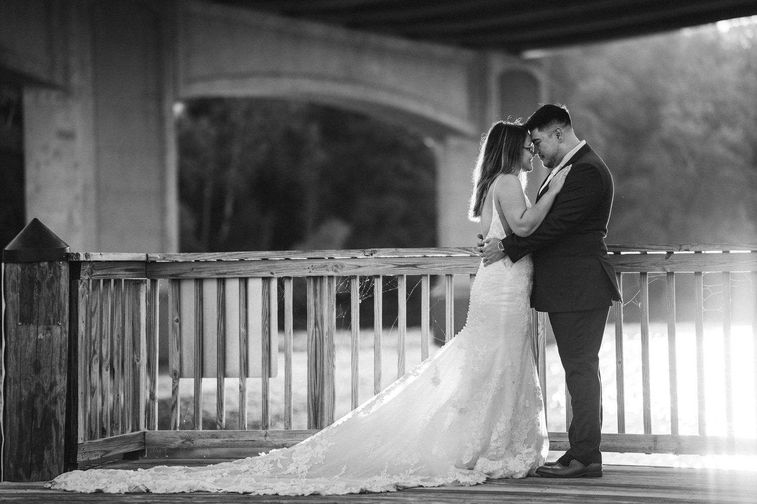 A black and white wedding photo of newlyweds embracing on a covered bridge with a flowing bridal gown.