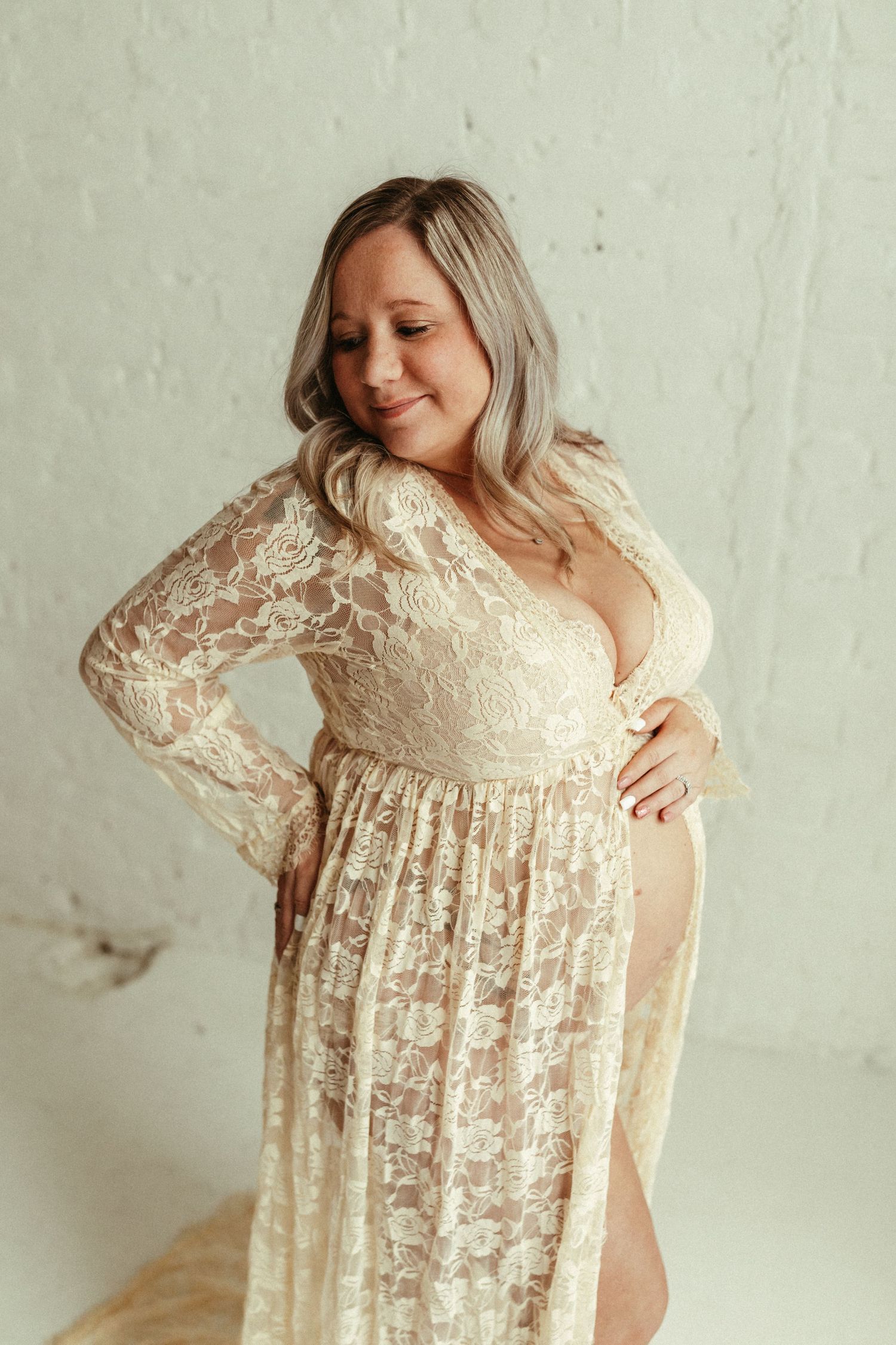 Pregnant woman showcasing a delicate cream-colored lace dress against a white backdrop in different poses and angles.