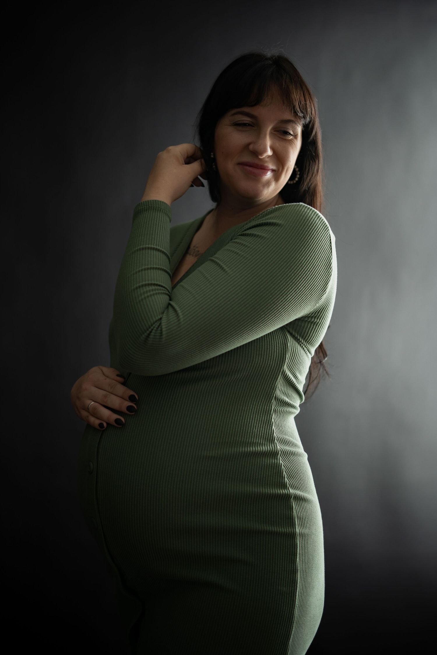 Maternity photo series showing a pregnant woman in green sweater against dark background.