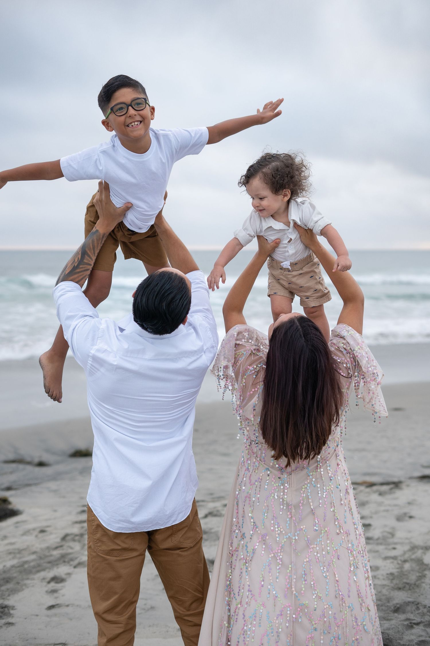 Playful couple in white and khaki twirls and dances together on a cloudy beach.