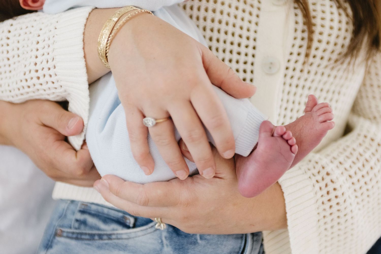 Close up of tiny baby foot with parent's hands and jewelry.
