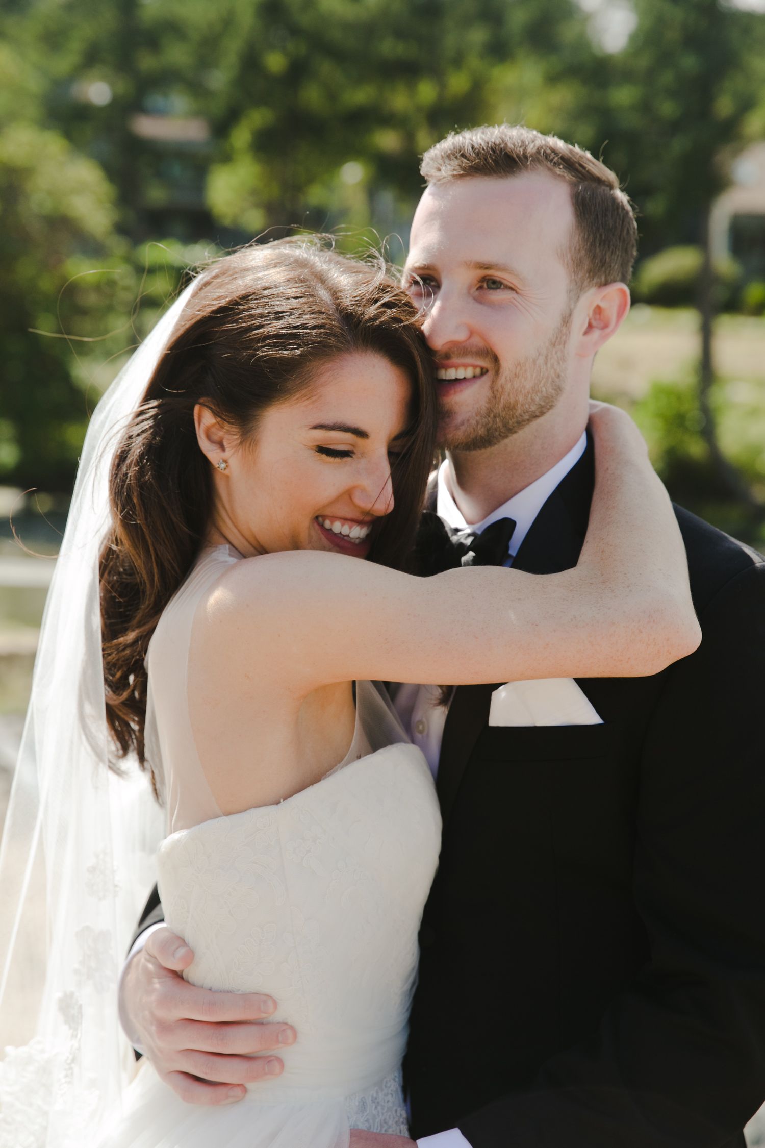 A happy couple shares a joyful moment on their wedding day, bride in white gown and groom in black tuxedo embracing outdoors.