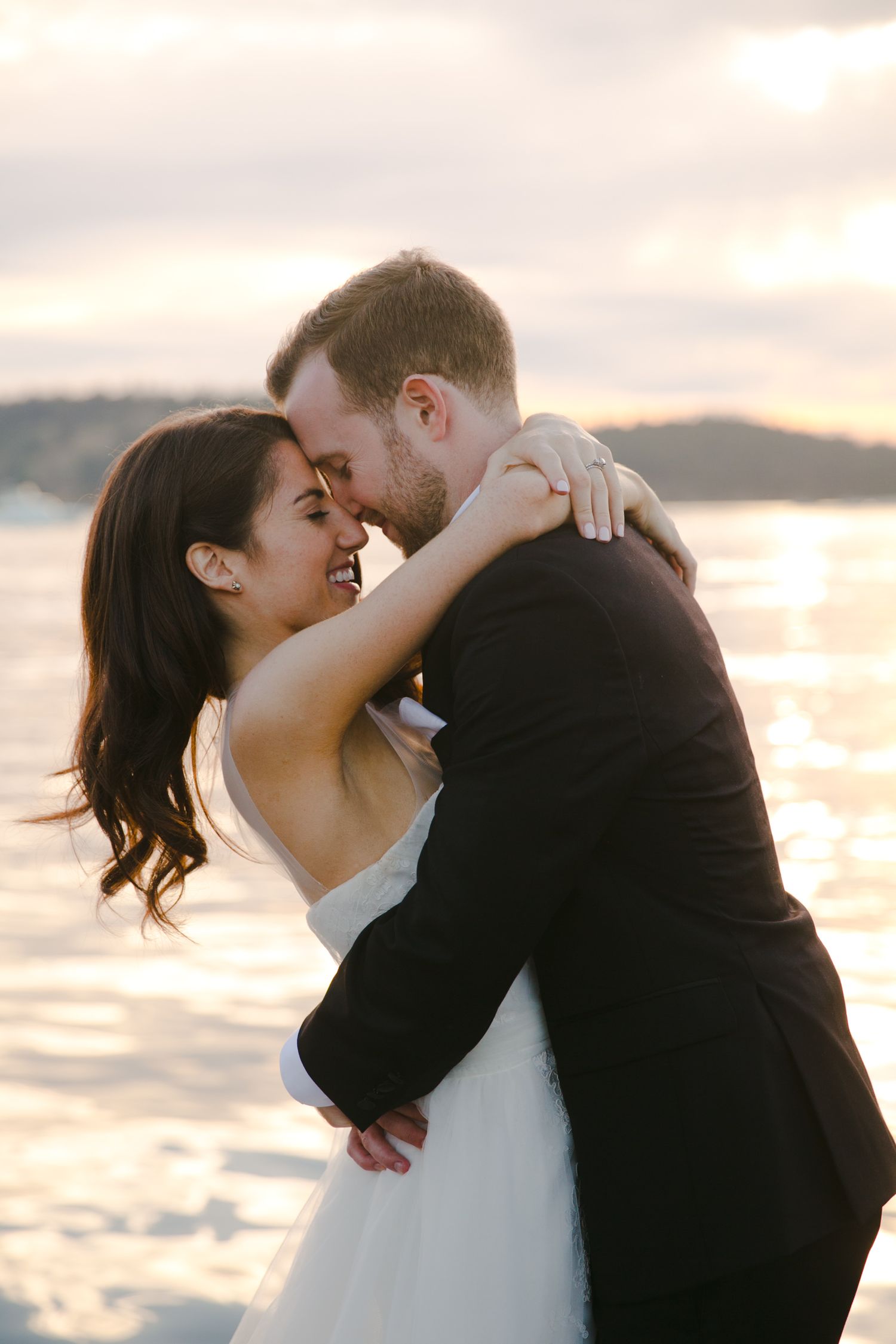 A romantic sunset embrace between newlyweds on a beach with glowing golden light reflecting off the water.