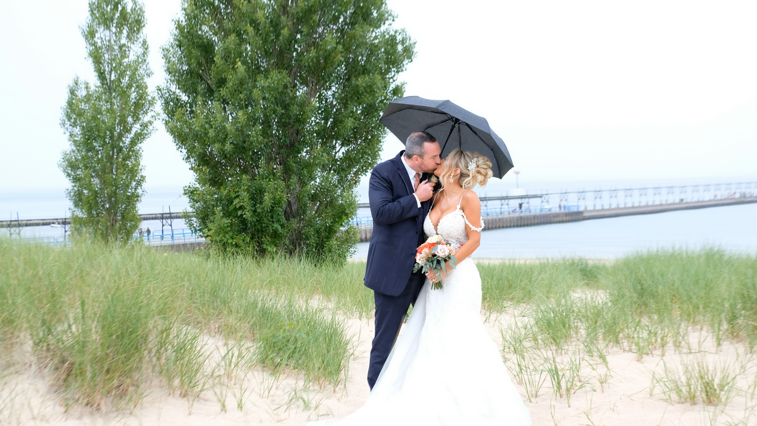 A newly married couple sneaking a kiss while under a umbrella on a beach.