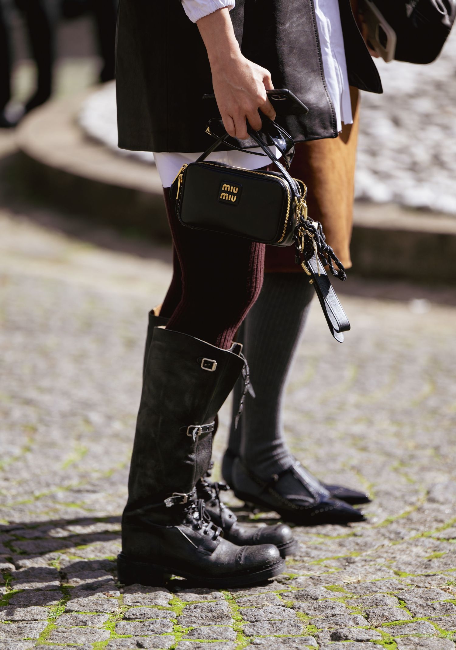 Close-up detail shot of black combat boots and small leather handbag on cobblestone street.