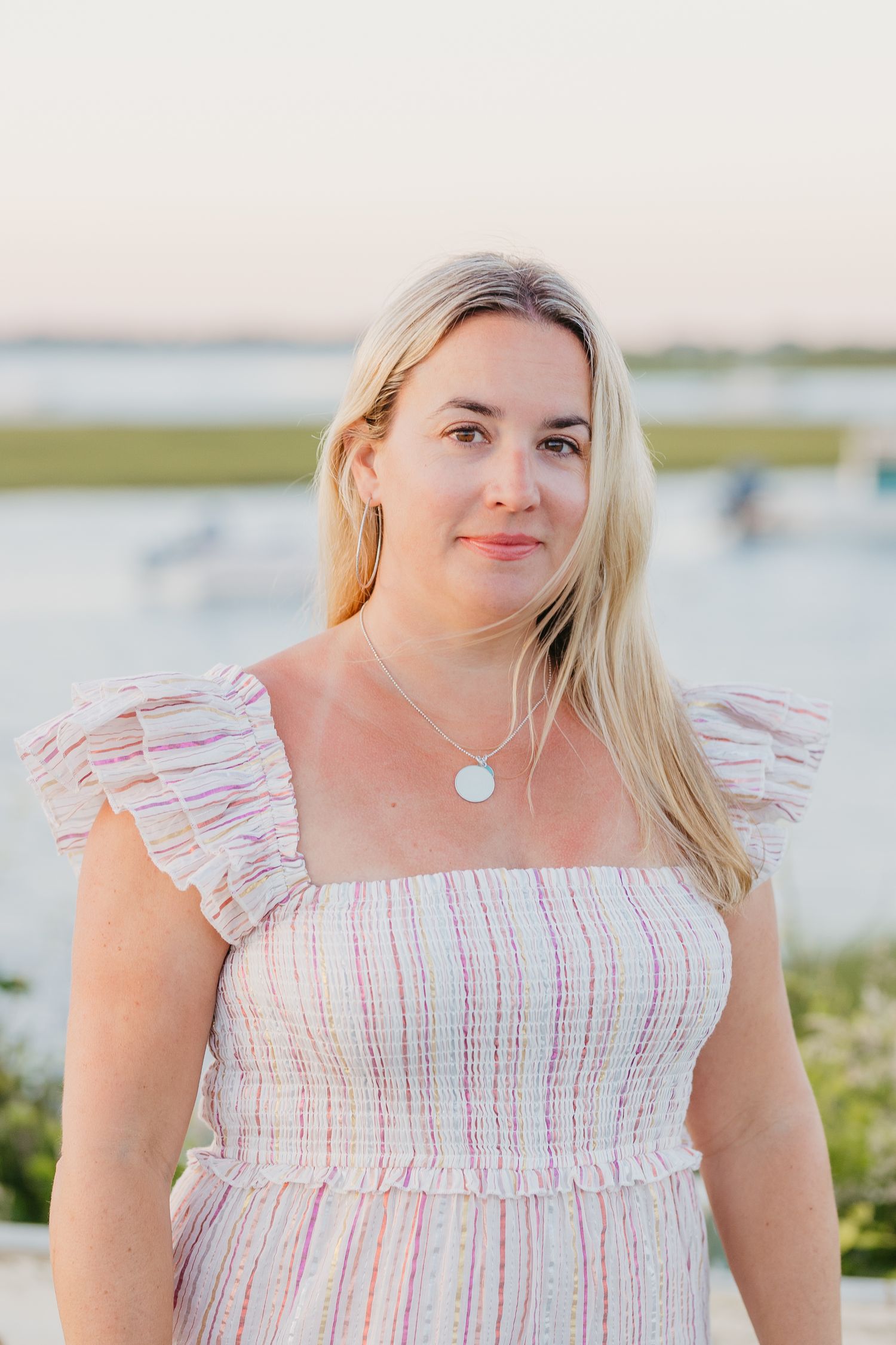 A portrait of someone wearing a striped sundress against a coastal backdrop at sunset.
