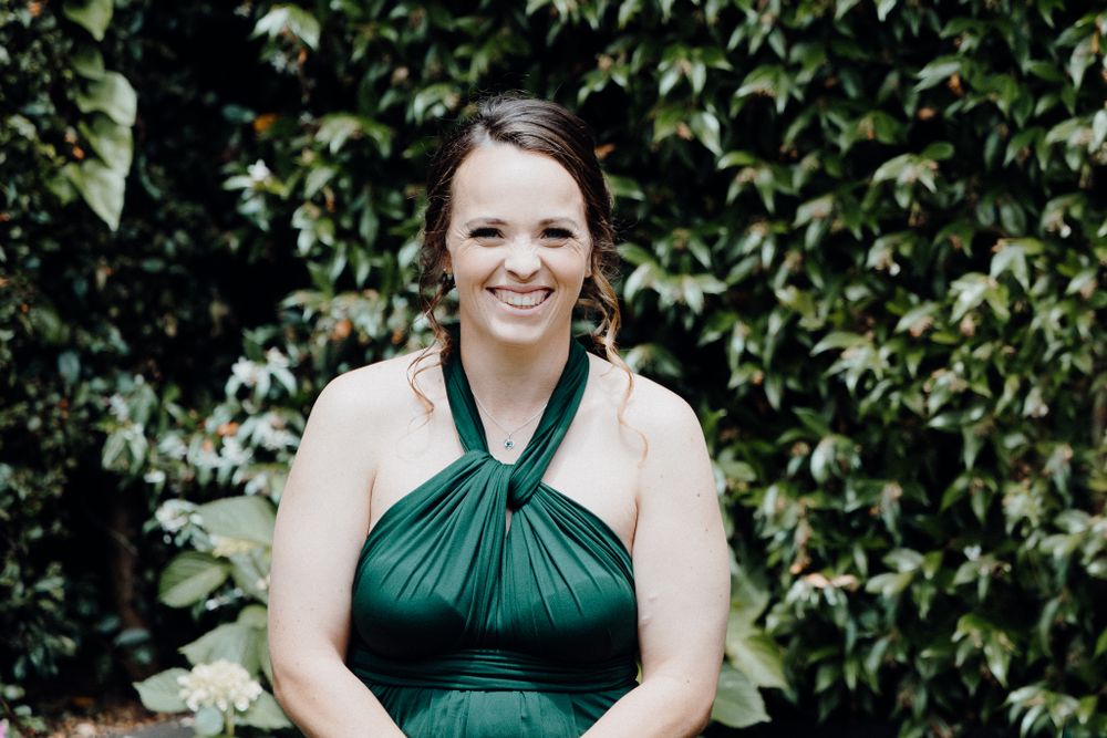 The Bridesmaid in an emerald green halter dress smiles as she sees the bride, captured by Apertured Media Auckland Wedding Photographer.