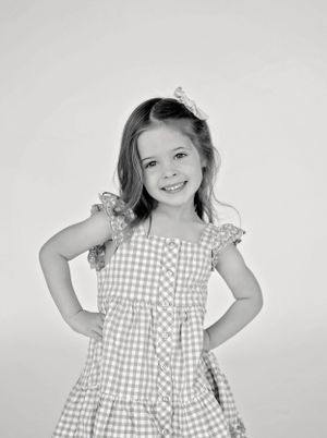 A child wearing a gingham dress strikes a fun pose against a white backdrop.