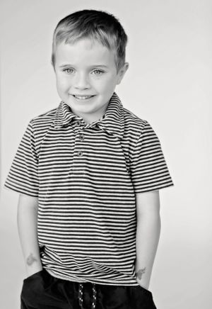 Black and white portrait of young child in striped polo shirt smiling at camera.