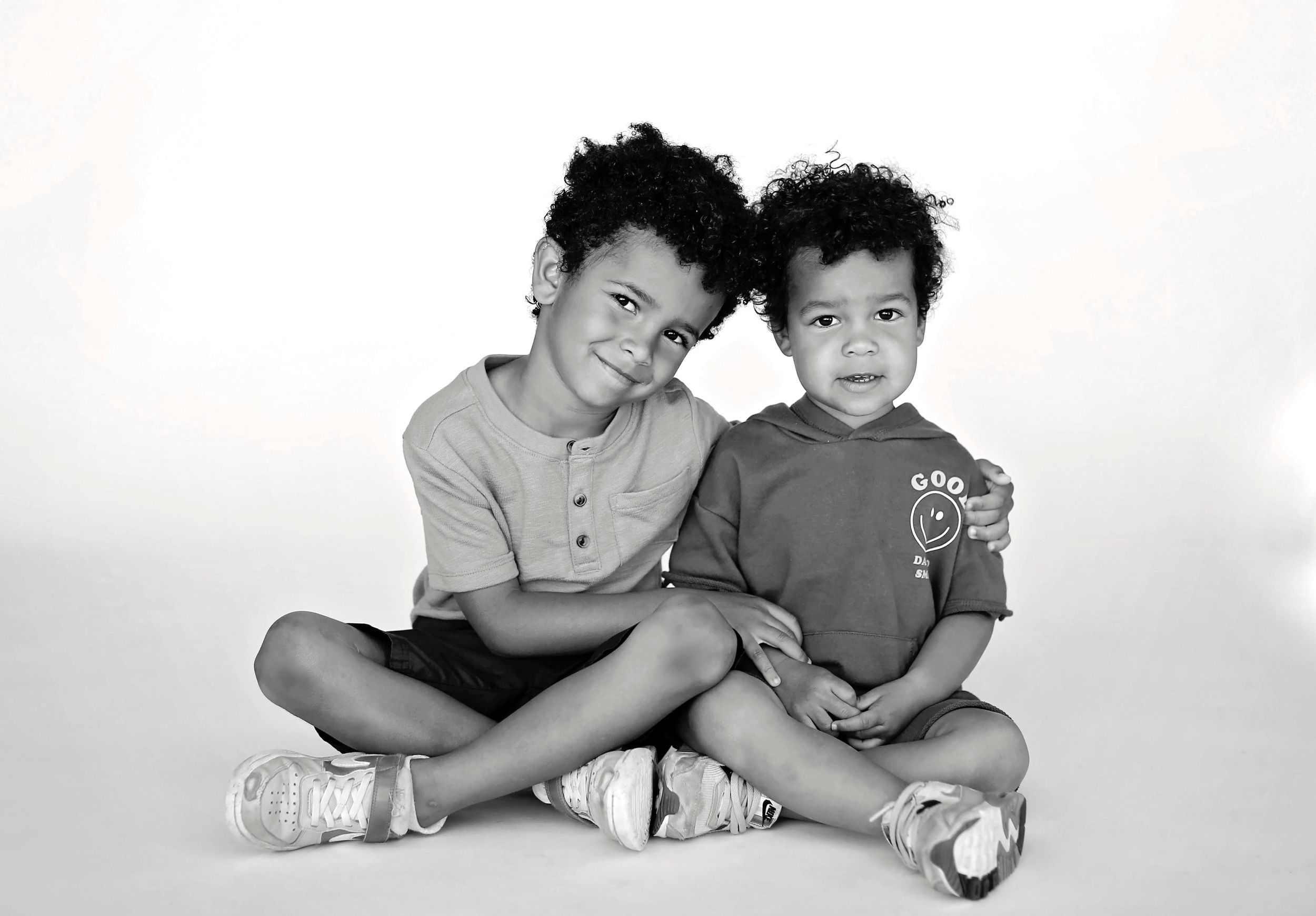 Black and white studio portrait of two children sitting together on floor.