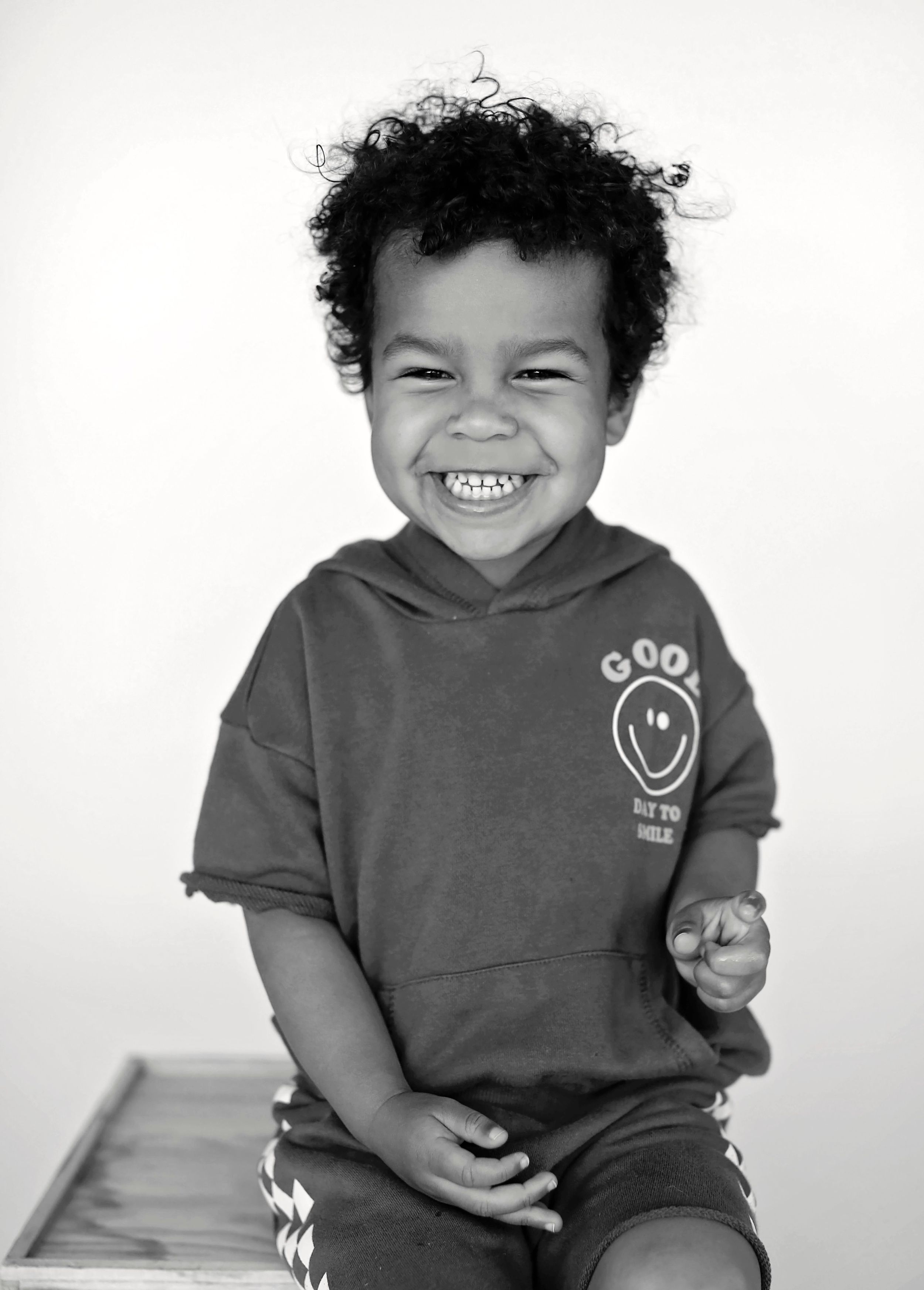 Black and white photo of child wearing hooded sweatshirt with big joyful smile.