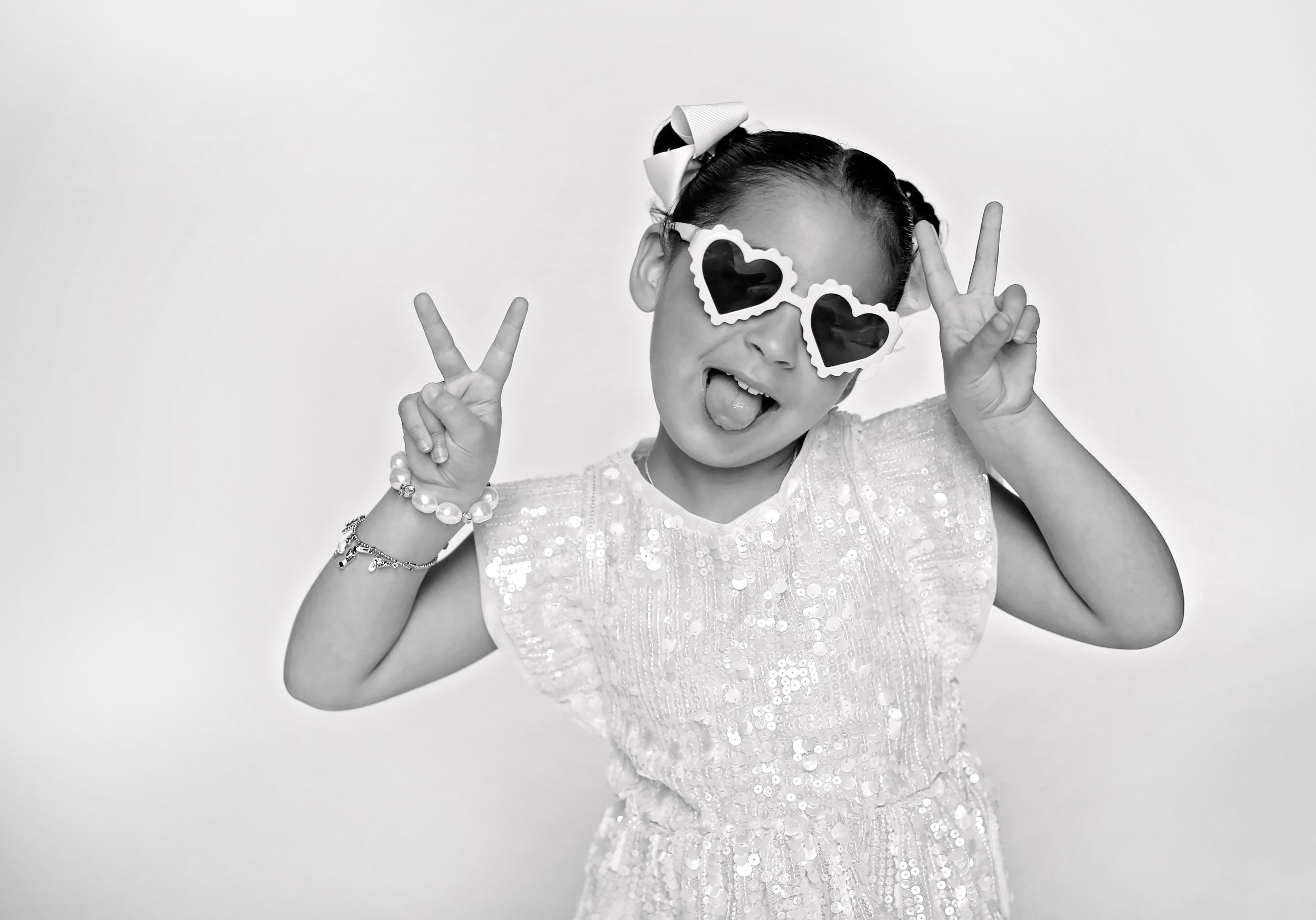 Black and white photo of child wearing heart sunglasses making peace signs.