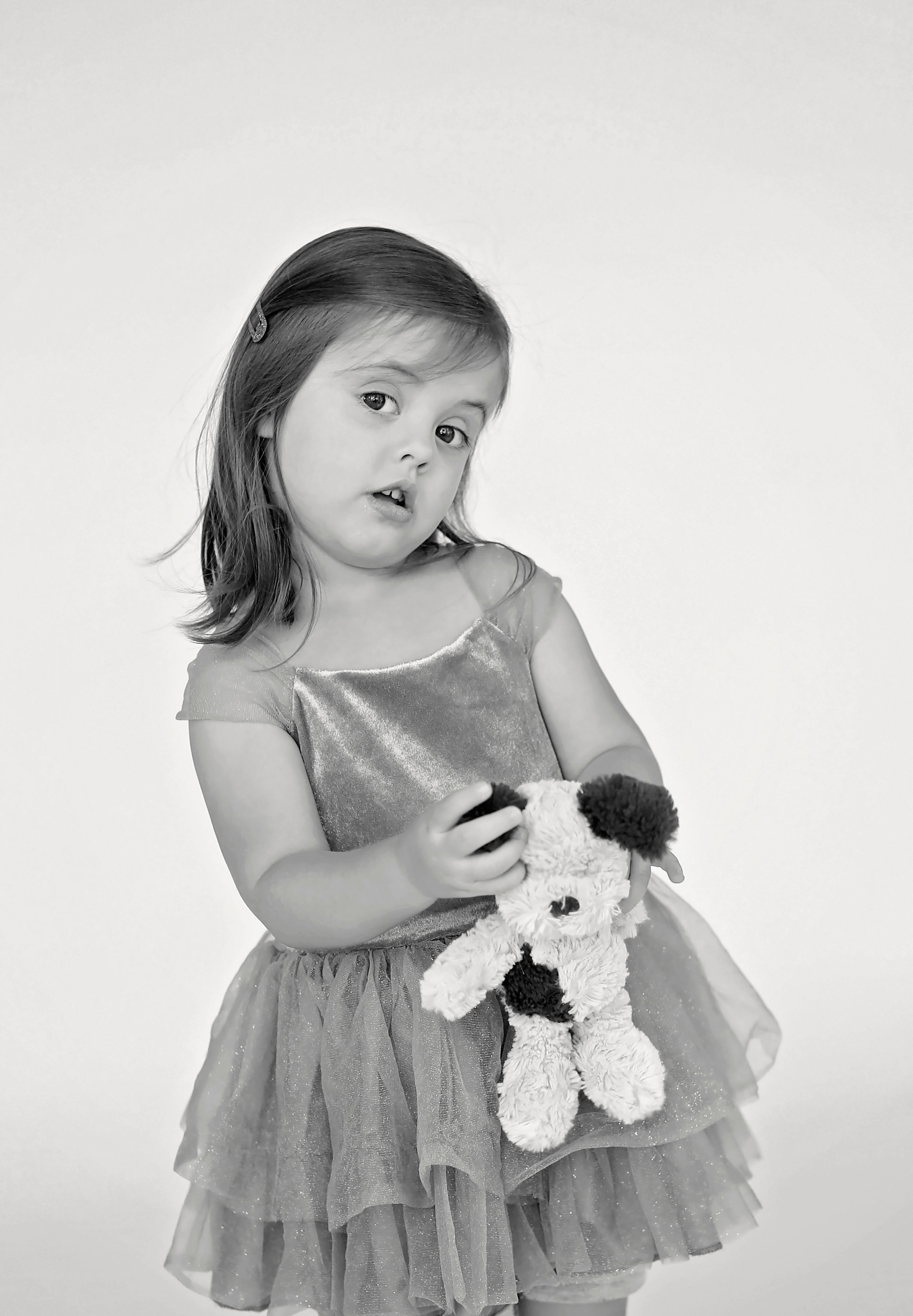 A child in a grey tulle dress holds a plush toy against a white background.
