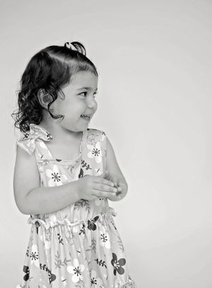 A toddler in a white floral dress twirls and plays in a series of black and white artistic photographs.