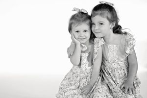 Black and white portrait of two young children in floral dresses sitting close together.
